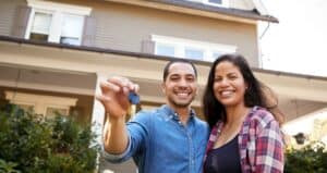 couple holding keys and smiling in front of new home
