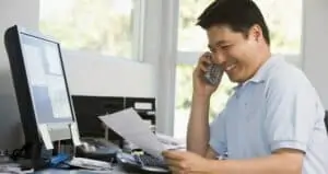 man on phone smiling in front of computer