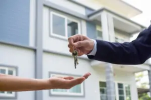 man handing keys to new homeowner with blue and white home in background