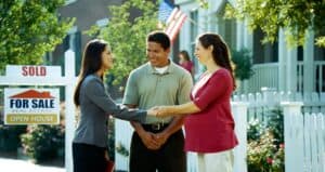 couple shaking hands of realtor in front of for sale and sold signs