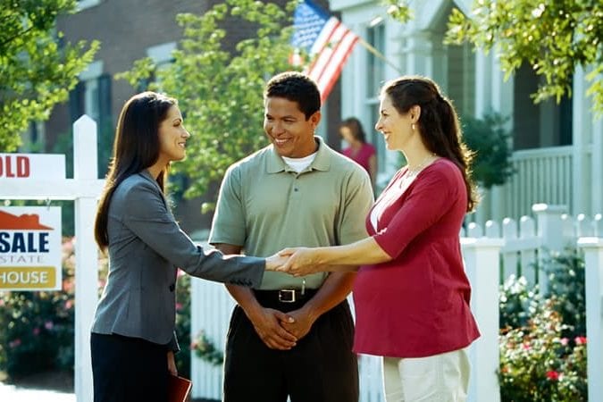 couple shaking hands of realtor in front of for sale and sold signs