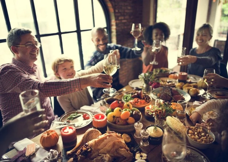 people around table for thanksgiving smiling, toasting each other with wine glasses in hand